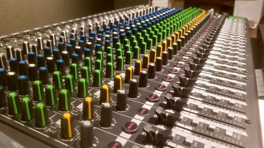 Audio mixing console with rows of colored knobs and sliders
