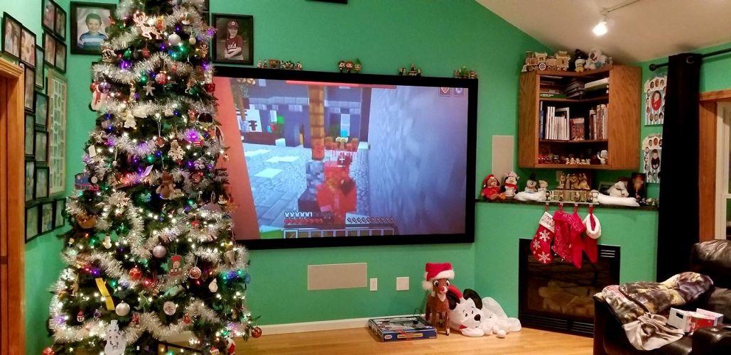 Living room with a Christmas tree and a large screen showing a game